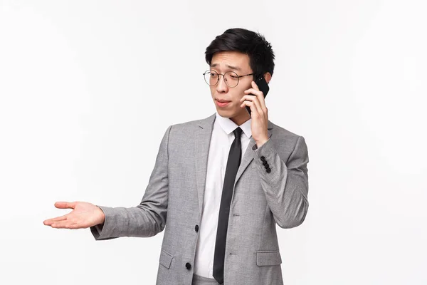 Περιμένετε-up πορτρέτο της σοβαρής αναζητούν δύσπιστοι νεαρός ασιάτης επιχειρηματίας να δώσει συμβουλές στο τηλέφωνο, έχοντας σημαντική κλήση από τον πελάτη, μιλώντας στο smartphone, gesturing χέρι και γκριμάτσα αναποφάσιστη — Φωτογραφία Αρχείου