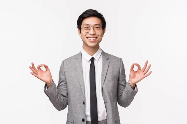 Keep calm and stay healthy. Handsome cheerful smiling asian male entrepreneur, office worker staying calm, holding hands in zen gesture, relaxing, meditating, white background