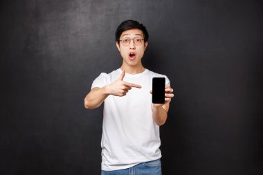 Teknoloji, aletler ve insan konsepti. Etkileyici ve heyecanlı Asyalı adam uygulamayı indirmesini, kontrol etmesini ve akıllı telefon ekranını göstermesini söylüyor.
