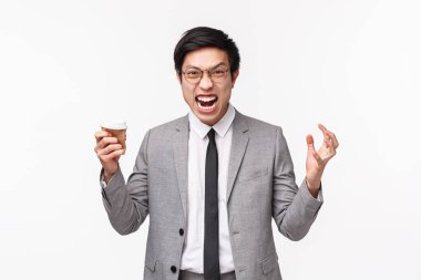 Ofis çalışanları, iş ve yaşam tarzı konsepti. Öfkeli, öfkeli, agresif Asyalı genç adamın belden aşağısı portresi kötü haberleri duyuyor, sinirden kuduruyor, deli gibi bağırıyor, yumruğunu sıkmış ve elinde bir fincan kahve tutuyor.