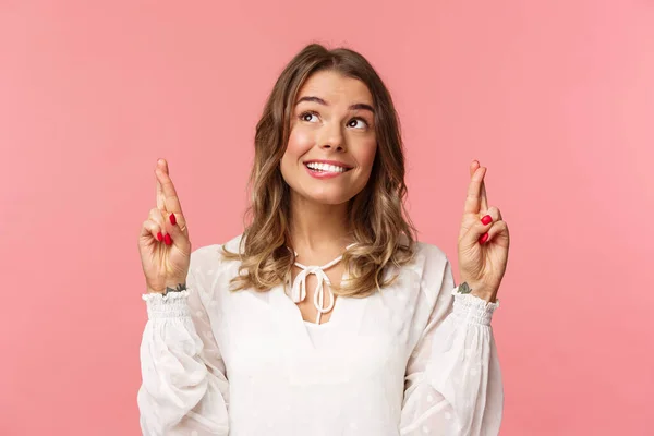 Close-up retrato de esperançoso, otimista mulher atraente em vestido branco, morder lábio e sorrir como sonhar acordado, sonho de esperança se tornar realidade, fazendo desejo ou oração, de pé fundo rosa — Fotografia de Stock