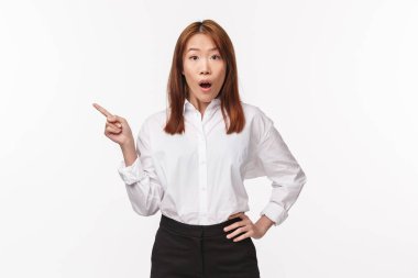 Şaşırmış ve şaşırmış Asyalı bir kadının portresi yakınlarda ilginç bir olay duyuyor, sola bakıyor ve kameraya bakıyor, orada ne olduğu hakkında sorular soruyor, beyaz arka planda duruyor.