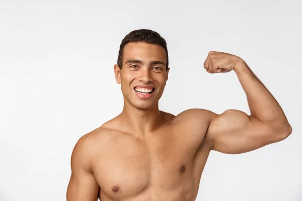 Adolescente afroamericano muestra músculos en el brazo. Aislado sobre fondo blanco. Retrato de estudio. Concepto de edad transitoria . — Foto de Stock