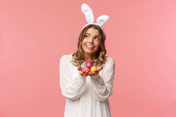 Vacances, printemps et concept de fête. Portrait de mignonne et tendre, belle femme blonde célébrant le jour de Pâques regarder rêvé avec sourire heureux, tenant Pâques œufs peints, porter des oreilles de lapin — Photo