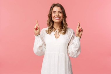 İyimser, genç, umut verici sarışın kızın portresi. Dileğini gerçekleştiriyor ve gerçekleşeceğini biliyor. İyi şanslar, gülümseyen kamera iddiası, rüya görmek için dua etme, pembe arka plan.