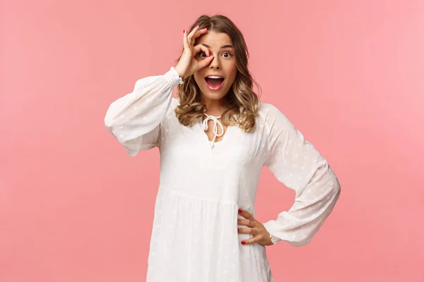 Retrato de asombrada y fascinada, sorprendida joven rubia ver algo realmente fresco, mirar con la cara emocionada y feliz, sonriendo encontrado lo que busca, mirar a través de signo de bien sobre el ojo — Foto de Stock