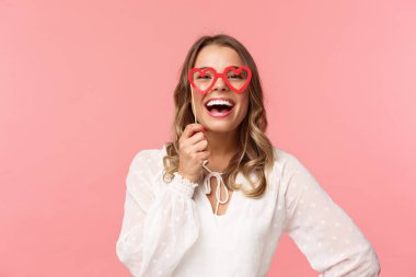 Bahar, mutluluk ve kutlama konsepti. Komik ve kaygısız, güzel beyaz saçlı, beyaz elbiseli, kalp şeklinde maske takan ve kahkahalar atan beyaz kadın portresi.