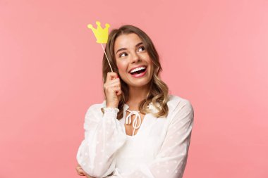 Bahar, mutluluk ve kutlama konsepti. Hayalperest genç sarışın kızın yakın plan portresi sevimli ve romantik bir şey, gülümseyen bir bakış çubukta taç ve pembe arka planla hayal kuruyor.