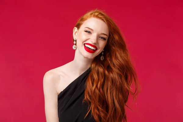Makyaj, güzellik ve kadın konsepti. Kırmızı arka planda dikilen muhteşem ve şık kızıl saçlı kadın portresi ruj, kahkaha, havada uçuşan kızıl saçlar. — Stok fotoğraf