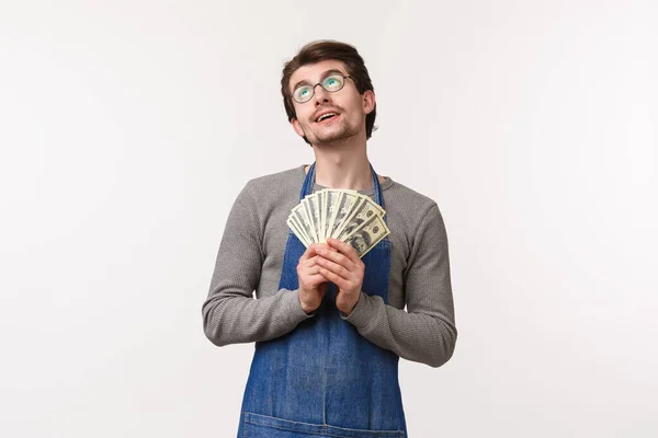 Concepto de pequeña empresa, finanzas y carrera. Retrato de hombre guapo encantado de ensueño en delantal, empleado recibe su cheque de pago, la celebración de dinero ganado y soñando con vacaciones, fondo blanco — Foto de Stock