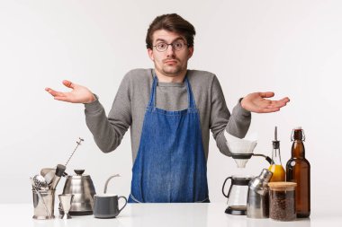 Barmen, kafe çalışanı ve barmen konsepti. Kafası karışık, kararsız, kafası karışık bir gencin portresi. Cevap veremiyor. Elleri yana açık omuz silkiyor, kafe tezgahının yanında duruyor.
