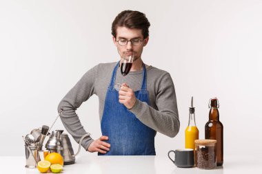 Barista, cafe worker and bartender concept. Portrait of elegant and serious-looking young male in apron sommelier tastes new flavour of wine, sniff smell of drink from glass with closed eyes clipart