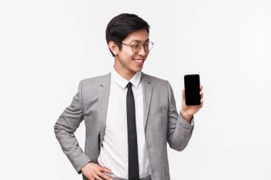 Gururlu Asyalı genç ofis çalışanının belden yukarı portresi, girişimci cep telefonu uygulamasını tanıtır, tatilden fotoğraflar gösterir, akıllı telefon ekranı, beyaz arka plan