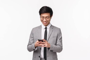 Yakışıklı, başarılı, Asyalı genç girişimcinin cep telefonu kullanan, kız arkadaşına mesaj atan, akıllı telefon ekranına gülümseyen, komik videolar izleyen, beyaz arkaplan...