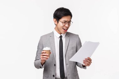 Ofis çalışanları, iş ve yaşam tarzı konsepti. Şok olmuş ve ürkmüş genç Asyalı girişimcinin belden yukarı portresi. Çalışan raporunu okuyor, huşu içinde kağıda bakıyor, kahveyi tutuyor.