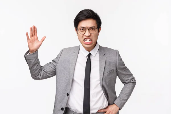 Cintura-para arriba potrait de enojado, indignado asiático hombre de negocios regañando a los empleados, gritando y levantando la mano agresivo, haciendo muecas con odio, siendo furioso de pie en traje sobre fondo gris —  Fotos de Stock