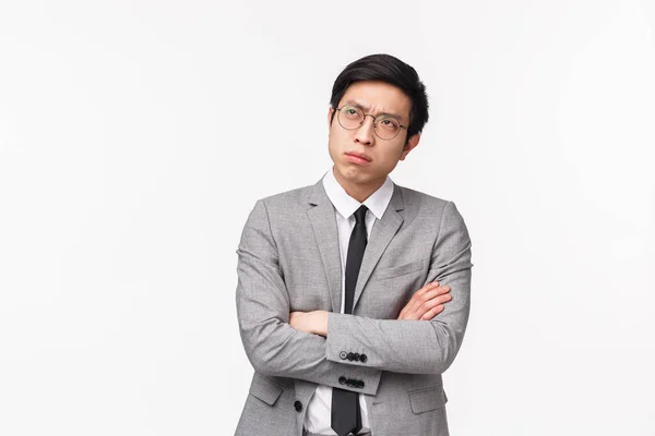 Waist-up portrait of puzzled, serious-looking asian guy in grey suit, looking up frowning and squinting thoughtful, cross hands chest, trying make-up solution, making choice indecisive