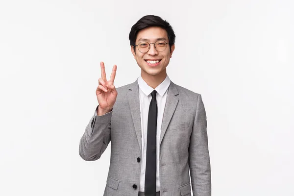 Midja upp porträtt av söta glada asiatiska manliga kontorsarbetare, bära grå kostym och slips, visar fred kawaii tecken, strålande leende optimistisk, att ha tillit till företagets välstånd, vit bakgrund — Stockfoto