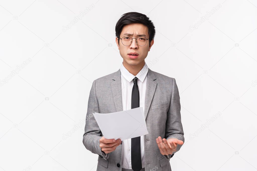 Waist-up portrait of skeptical, serious-looking asian businessman scolding employee for strange bad report, holding documents looking at camera frustrated and confused, white background