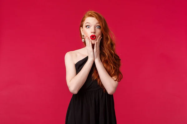 Concepto de moda, lujo y belleza. Divertido e interesado, sorprendido mujer joven elegante en vestido de lujo negro, labios plegables de la cara del tacto asombrado, chismes en la fiesta, fondo rojo — Foto de Stock