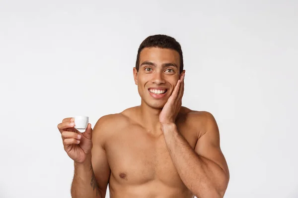 Fénykép félmeztelen afro-amerikai férfi mosolygós és alkalmazása arckrém elszigetelt fehér háttér — Stock Fotó