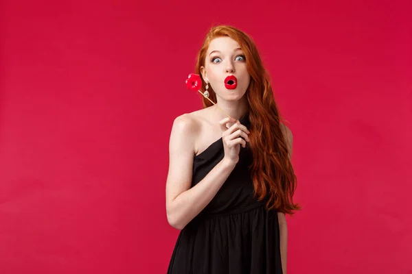 Πορτρέτο της κομψής κομψή κοκκινομάλλα γυναίκα σε μαύρο φόρεμα, πτυσσόμενα χείλη σε διασκέδαση και αναζητούν ενθουσιασμένοι, κρατώντας τα χείλη χαρτόνι, στέκεται κόκκινο φόντο, διασκεδάζοντας για τα κορίτσια κόμμα — Φωτογραφία Αρχείου