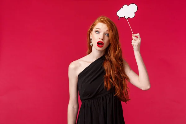 Retrato da mulher ruiva feminina atraente indolente e indecisa em vestido preto, segurando cartão de comentário nuvem sobre a cabeça como se não tivesse ideias, não pode pensar plano olhar sombrio, fundo vermelho — Fotografia de Stock