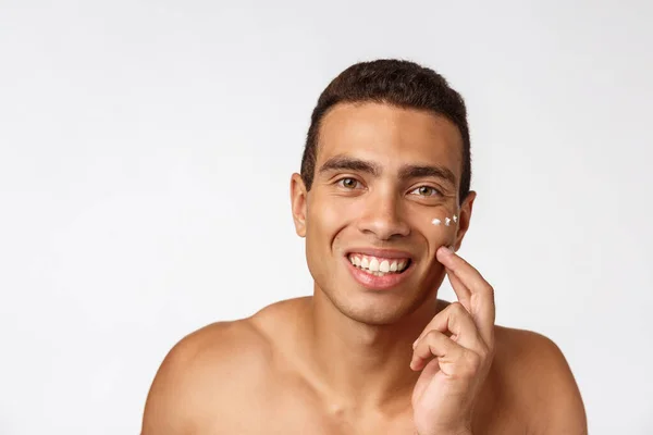 Fénykép félmeztelen afro-amerikai férfi mosolygós és alkalmazása arckrém elszigetelt fehér háttér — Stock Fotó
