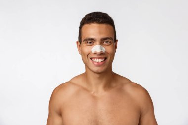 Yakışıklı Afrikalı Amerikalı adam siyah nokta ve kırışıklıkları azaltmak için burun bandı kullanıyor, duş bonesi takıyor, geniş bir gülümseme takıyor..