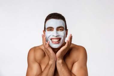 Kamerada gülümseyen neşeli, genç bir Afrikalı adam resmi. Yanaklarında krema maskesi olan bir adamın portresi. Güzellik rutini