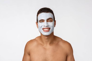 Kamerada gülümseyen neşeli, genç bir Afrikalı adam resmi. Yanaklarında krema maskesi olan bir adamın portresi. Güzellik rutini