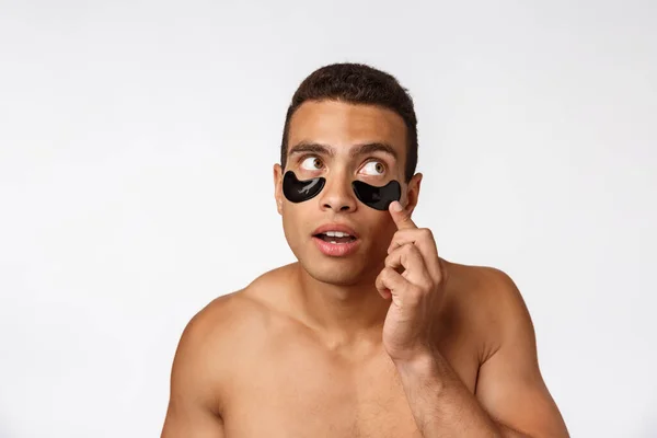 Vonzó afrikai fiatalember szem alatt fekete foltok gondoskodó arcbőre egyenesen a kamerába szürke háttér — Stock Fotó