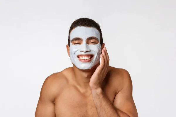 Foto van een vrolijke jonge Afrikaan die glimlacht op de camera. Portret van een man met een crème masker op zijn wangen. Schoonheidsroutine — Stockfoto