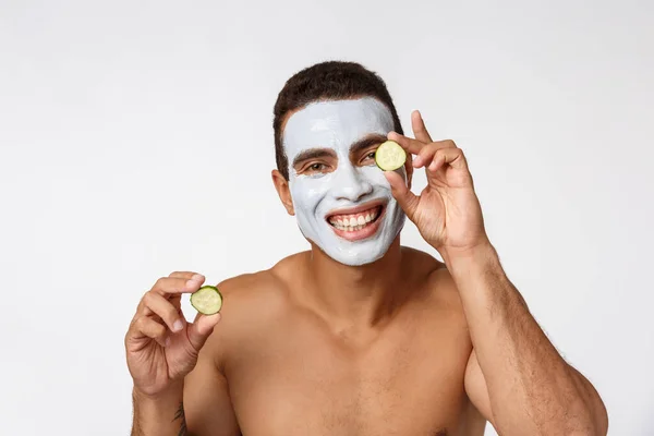 Fénykép vidám afro-amerikai férfi arc kozmetikai maszk gúnyolódik uborka elszigetelt fehér háttér — Stock Fotó
