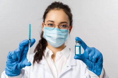 Doktorlar, enfeksiyon uzmanı, araştırma ve kovid19 konsepti. Genç Asyalı enfeksiyoncunun portresi, tıbbi maskeli kadın hemşire, eldivenler ve beyaz önlük, elinde Coronavirus 2019 aşısı şırıngası ve ampulü