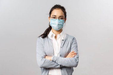 Covid19, virüs, sağlık ve tıp konsepti. Uzaktan kumandayla çalışan Asyalı genç bir işçinin portresi. Güvenli bir şekilde çalışıyor, tıbbi maske takıyor, göğsüne çapraz eller takıyor. Ciddi görünüyor.