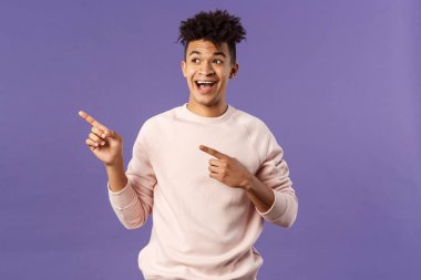 Neşeli, korkusuz, gülümseyen, üst sol köşesine bakıp işaret eden yakışıklı İspanyol adamın portresi. Ürün ya da şirket afişi, kopya alanı, mor arka plan.