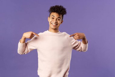 Şirin ve aptal yakışıklı erkek öğrenci kendini göstererek sevimli bir gülümseme sergiliyor. Katılmak veya seçilmek istiyor. Aday olmak için gönüllü, mor arka plan.