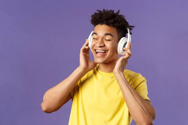 Primer plano retrato de despreocupado, joven optimista hombre con rastas, ojos cerrados y sonriendo complacido como escuchar nueva canción increíble artista favorito subido plataforma de música, usar auriculares —  Fotos de Stock