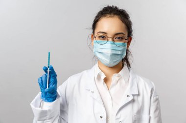 Doktorlar, enfeksiyon uzmanı, araştırma ve kovid19 konsepti. Ciddi Asyalı maskeli genç kadın hemşire portresi. Elinde virüsten, pandemiden, hastanedeki hastayı tedavi eden şırınga var.