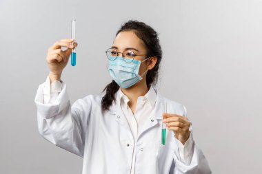 Doktorlar, araştırma ve kovid19 konsepti. Genç araştırmacı enfeksiyoncunun portresi, testlerin sonuçlarından memnun olan bilim adamı, aşıyla dolu şişeyi tutuyor, Coronavirus 'un tedavisini icat ediyor.