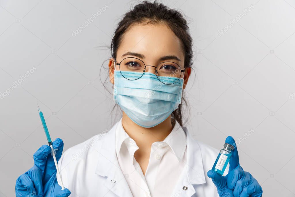 Doctors, infectionist, research and covid19 concept. Close-up of asian female nurse in medical mask, gloves and white coat, holding syringe and ampule with coronavirus vaccine, cure people