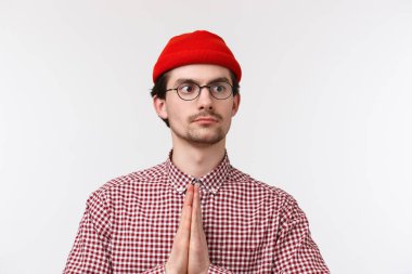 Yakın plan portre komik beyaz adam bıyıklı, kırmızı bereli ve gözlüklü, namaste ya da dua eden, ciddi kararlı bir ifadeyle beyaz arka planda duran,