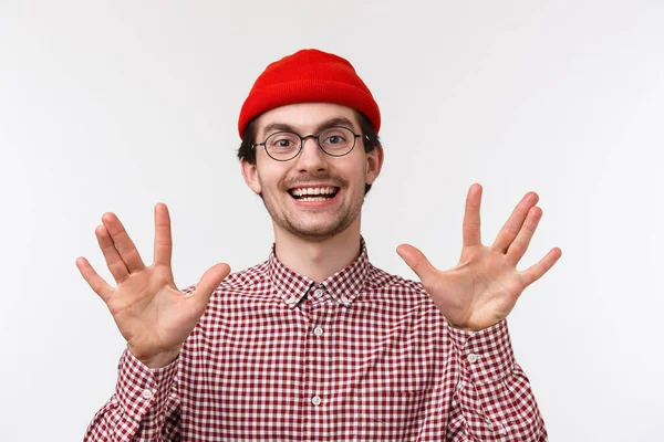 Närbild porträtt rolig hipster kille i röd mössa och glasögon gör spok gest visar fingrar och leende, diskutera favorit tv-serie med vänner nördar, stående vit bakgrund optimism — Stockfoto