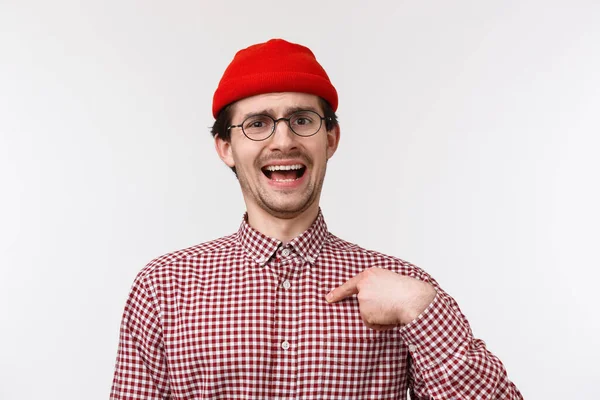 Närbild porträtt skrytsam rolig skäggig ung man i röd mössa och glasögon, pekar på sig själv som talar egna prestationer, skryta personliga mål, stående vit bakgrund — Stockfoto