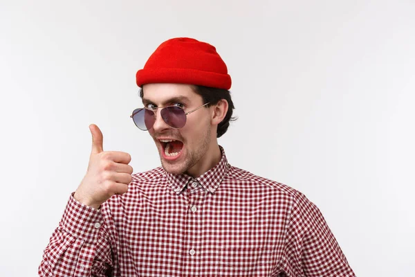 Beau et drôle excité jeune homme avec moustache, porter des lunettes de soleil et bonnet hipster rouge, montrant pouce vers le haut et la caméra de recherche encourager acheter des produits, travail ami louange satisfait — Photo