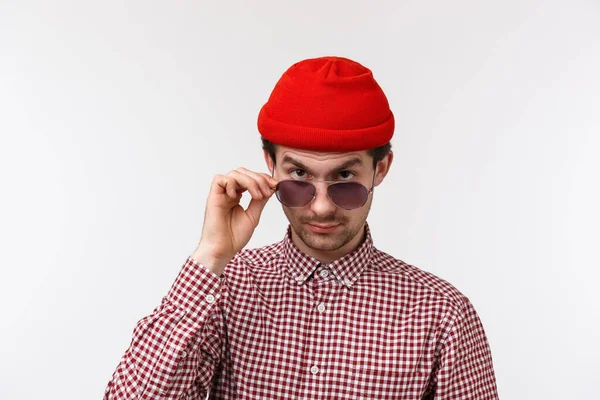Skeptický a pochybovačný pohledný hipsterský mladík s knírkem, červenou čepicí, dívá se zpod čela s nevírou, vzletovými brýlemi a vážně odsuzuje cizí osobu. — Stock fotografie