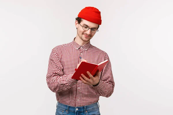 Portrait taille haute drôle mec barbu mignon bonnet rouge, lunettes, écrire des notes pendant la conférence, faire la liste des épiceries ou avoir un journal, sourire heureux de travailler sur le projet, fond blanc — Photo