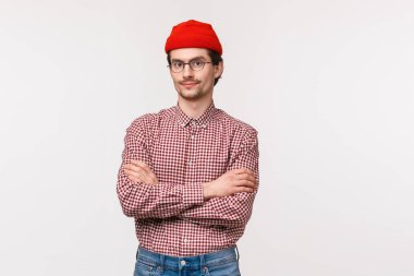 Belden yukarı portre, beyaz sakallı, gözlüklü, kırmızı bereli, elleri göğüstte, kamera karşısında hazır, profesyonel pozda, çalışanları kontrol altına alıyor.