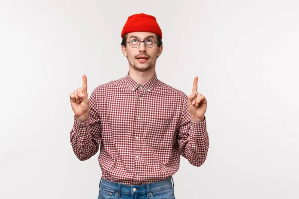 Midja upp porträtt roligt kreativ ung man med mousatche i glasögon och röd mössa, peka fingrar upp och rullande ögon till toppen som ser något coolt, stående vit bakgrund — Stockfoto